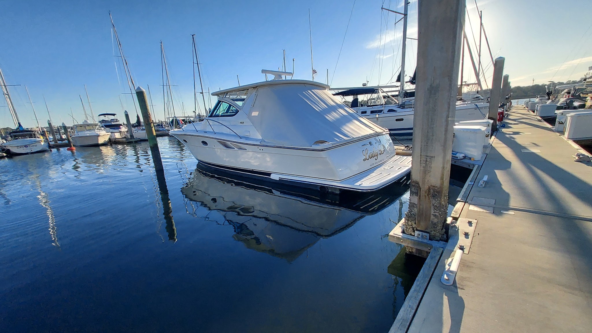 A cruiser at its slip with its hull reflected in still marina water