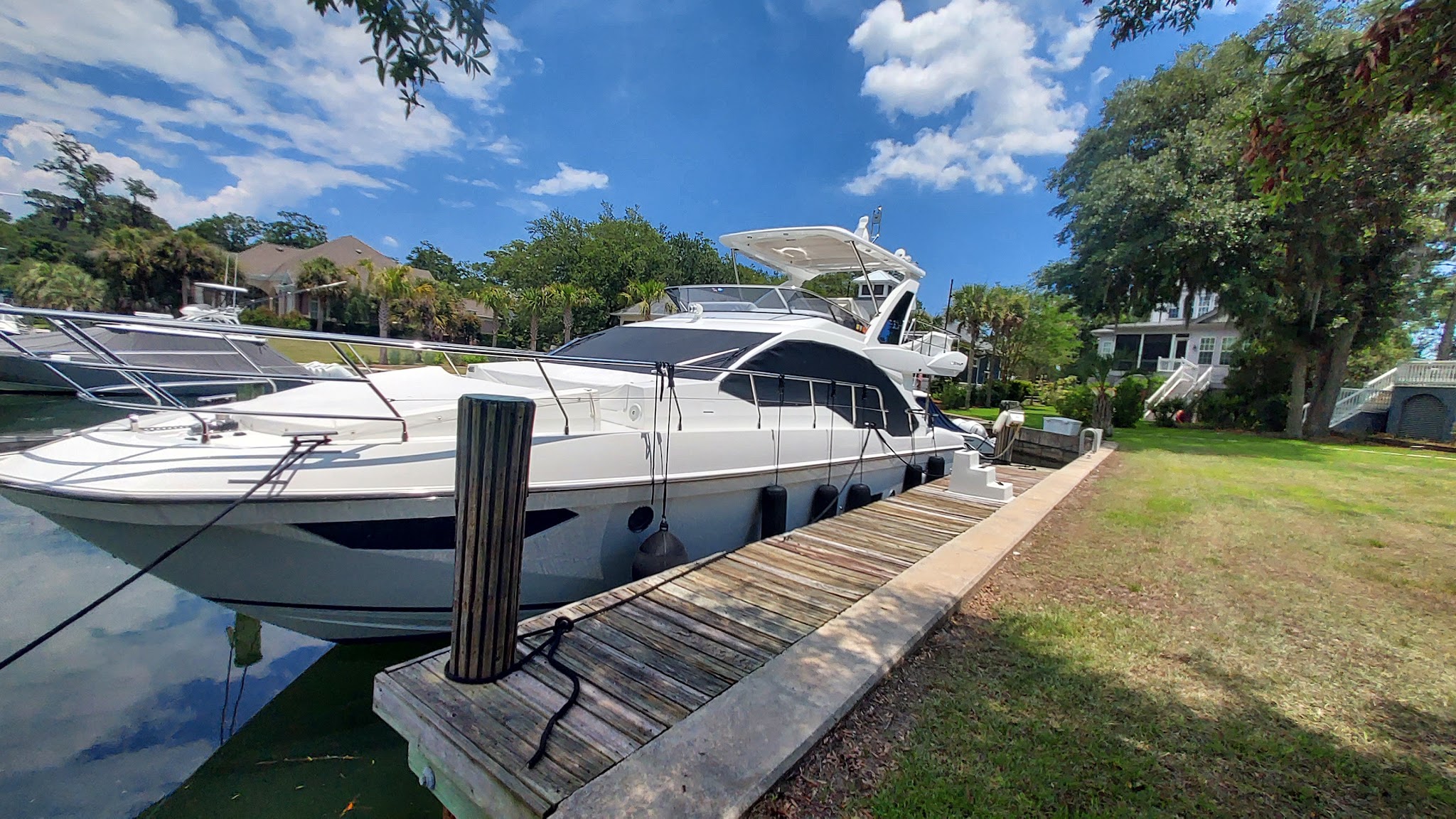 A flybridge yacht tied up at a private dock under a blue sky